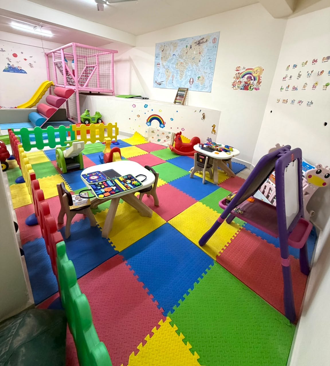 The Creative Corner at The Play Hive with activity tables, an easel, colourful soft flooring, and educational wall art